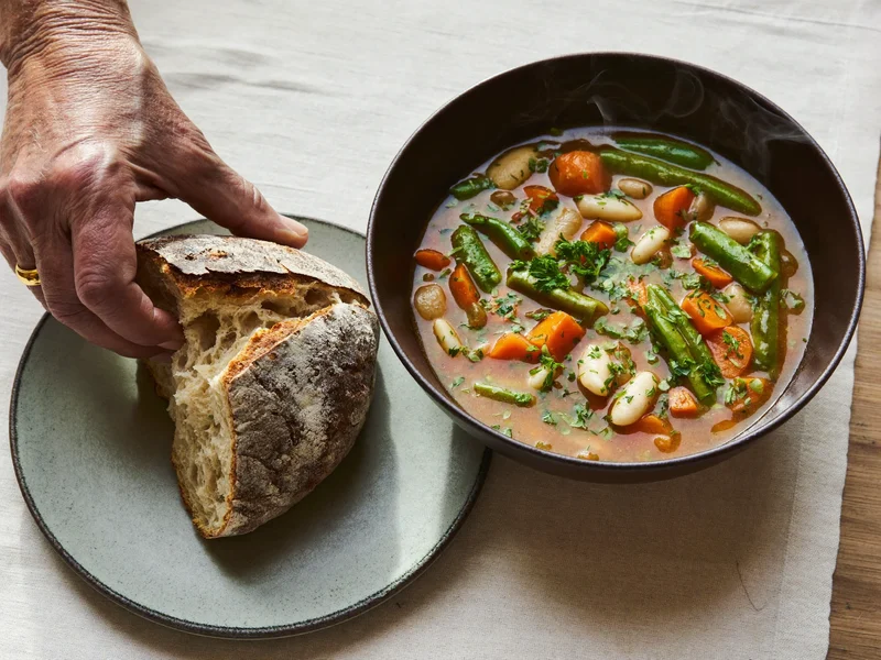 Zuppa di verdure fumante con pane rustico su tovaglia di lino