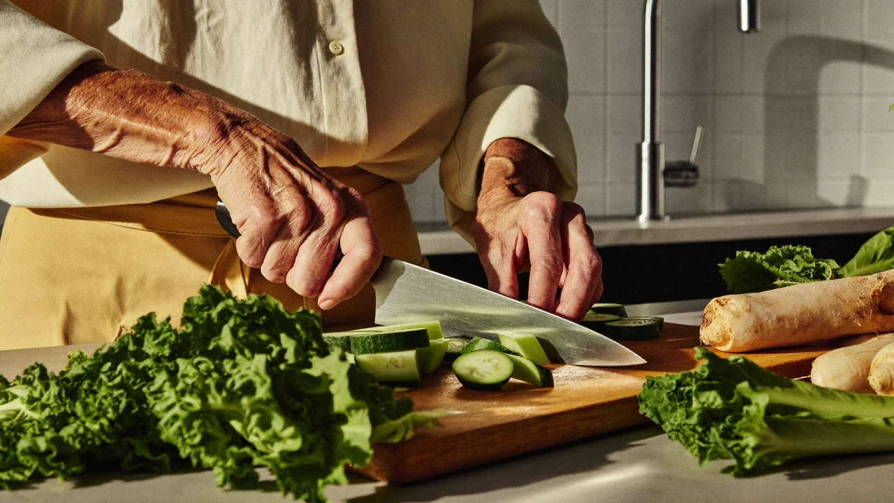 Mani anziane tagliano verdure su un tagliere in una cucina luminosa