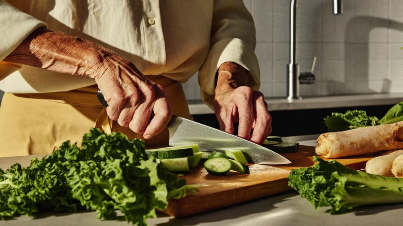 Mani anziane tagliano verdure su un tagliere in una cucina luminosa